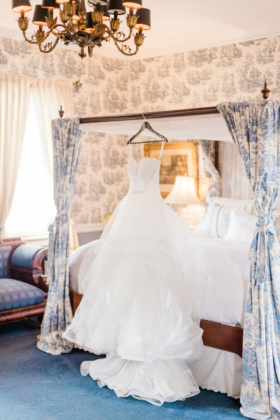 Wedding Dress hanging on a hanger above a beautiful country style bed at Antrim 1844