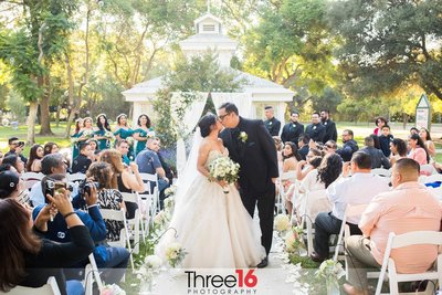 Bride and Groom stop on the aisle for their second kiss as guests look on at Heritage Park in Santa Fe Springs