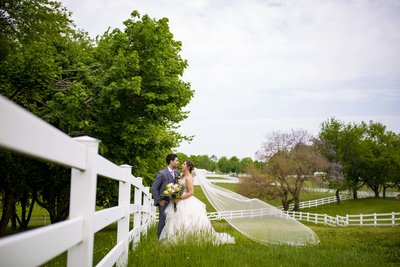 A bride and groom stand by a white picket fence.