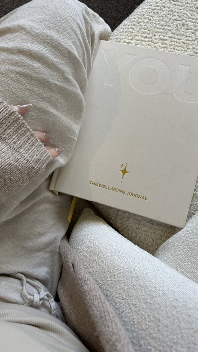 Minimalist flat lay of a cream-colored well-being journal and cozy loungewear, symbolizing mindfulness, mental health, and self-care practices