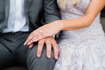 Wedding couple holding hands on lap displaying wedding rings