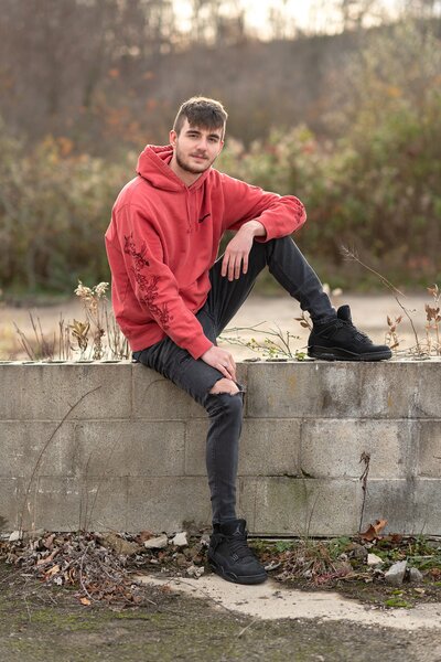 High school senior boy in red Supreme sweatshirt sitting on cinder block wall