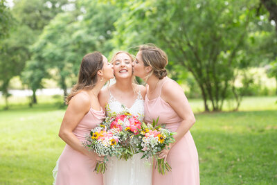 Two bridesmaids kiss their bride on her cheeks