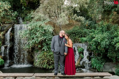 Groom to be whispers in his Bride's ear causing her to smile as they pose in front of a waterfall at the LA Arboretum