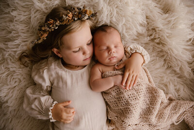 siblings freya and hugo holding each other and laying on a fluffy blanket during a newborn photoshoot with taranaki newborn photographer aimee kelly photography