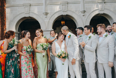 a groom kisses his bride's forhead as their wedding party laughs and cheers them on