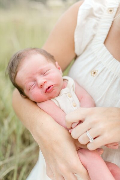 Mother holds infant child in Edina field for newborn photography session in Edina.