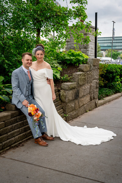 Bride and groom smiling together along stone path lined with greenery – photographed by wedding photographer Niko Coric – Lumen Clarity Media