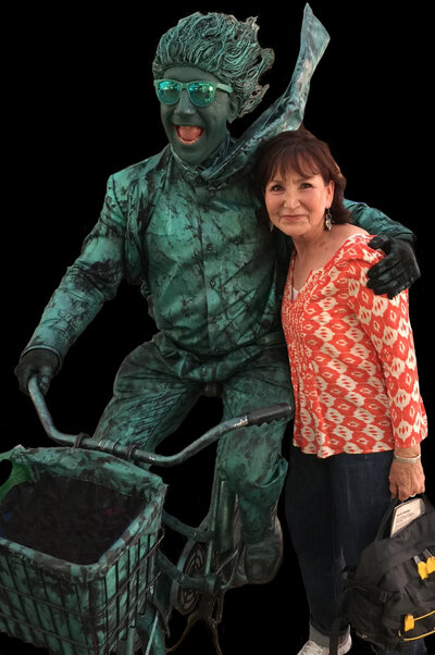 Charlotte Meares standing beside a green man on a bycycle, symbolizing her appeal to any kind of writer who needs her editing or ghostwriting services.