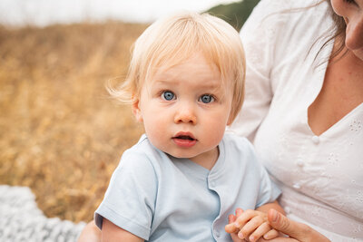 blue eyed baby stares inquisitively at camera from mums lap