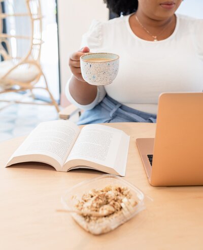 black lady ready book and opened laptop with a cup of coffee in hand
