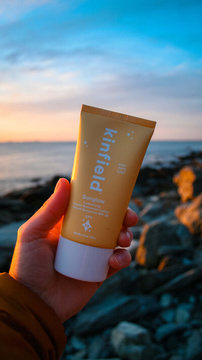 sunscreen in hand with a coastal view of the ocean at sunrise