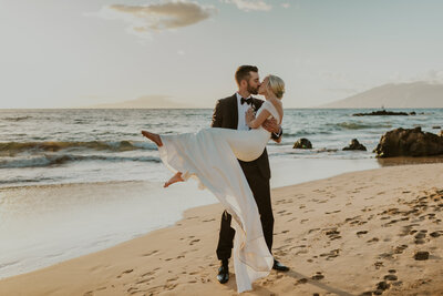 groom holding bride on the beach