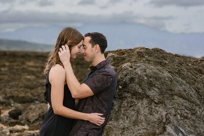 A man and a woman lean against a rock embracing romantically.