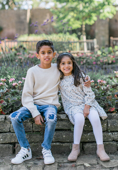 brother and sister sitting in a flower bed smiling during their London Family Mini Shoot with Philippa Sian Photography