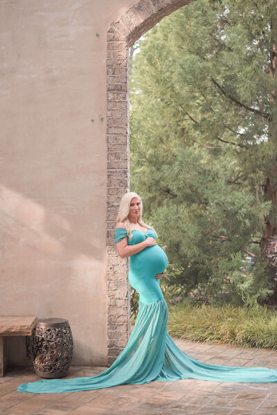 maternity session of a blond woman wearing a teal color long dress, she is standing on stairs