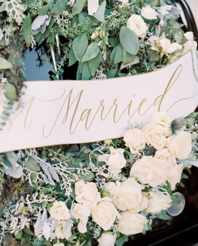 Hand-lettered just married banner on getaway car with white rose and greenery wreath