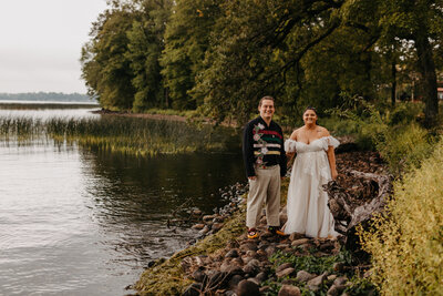 bride and groom smiling at the camera next to a lake