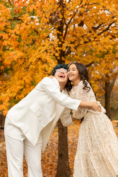 siblings hug and laugh in front of orange fall colors tree