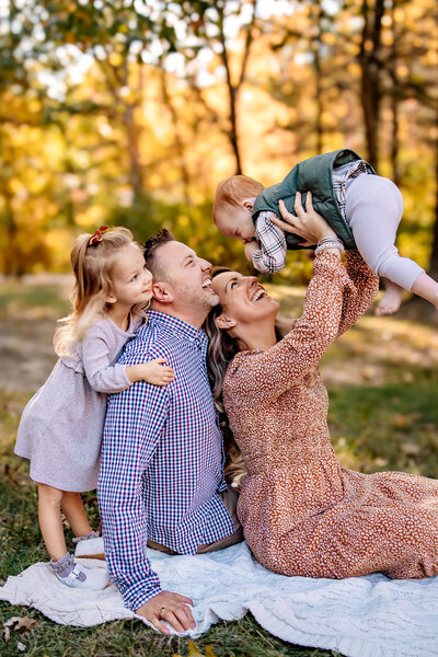 A family of 4  snuggled up together on a blanket while they pose for Family Portraits in a field of  The Grand Basin in Forest Park in St. Louis, Missouri.
