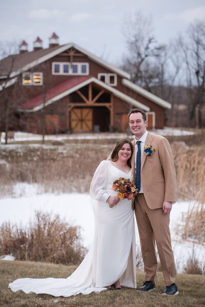 Bride and groom smile together outside Barnwood Events in Madison, Wisconsin, with the rustic barn venue in the background on a snowy winter day.