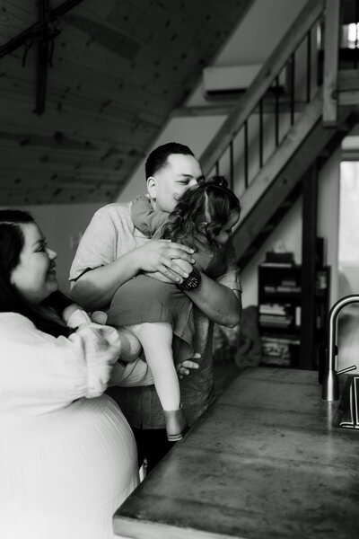 black and white photo of father cuddling toddler as pregnant mother watches