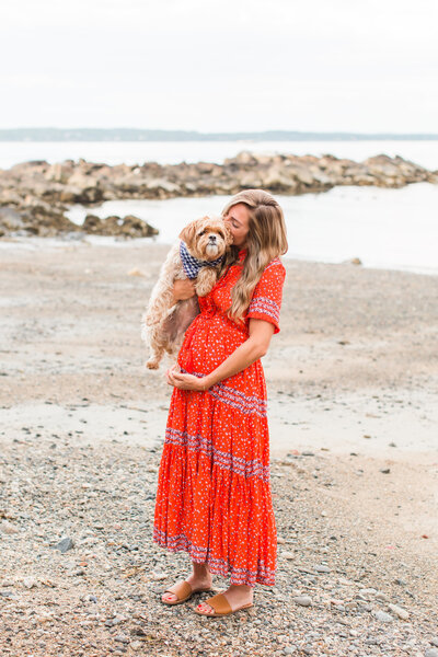 pregnant woman kissing her dog on a beach