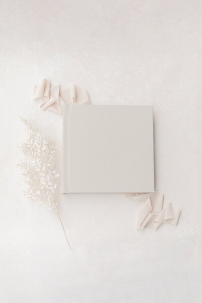 A cream photo album artfully displayed on ribbon with flowers next to it photographed by New Jersey Portrait Photographer Kate Voda Photography