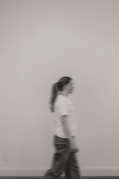 Creative branding photography capturing a woman walking in motion against a plain wall.