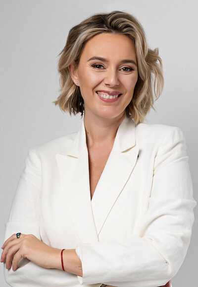 blonde short hair woman is wearing a white blazer and smiling to the camera for her headshot