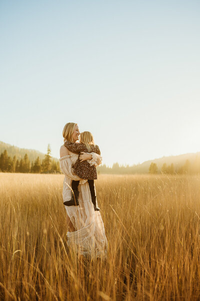Mom holding daughter  during golden hour in a field.
