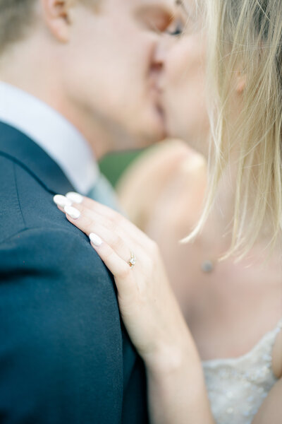 Detail shot of bride's wedding ring and hand on shoulder of the groom while they share a kiss on their wedding day