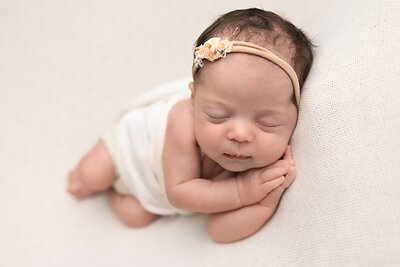 Baby girl on white backdrop with hands under cheek by portland photographer