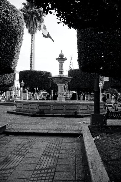 Black and white photo of the traditional plaza with a fountain in Lourdes's Mexican home state of Michoacan.