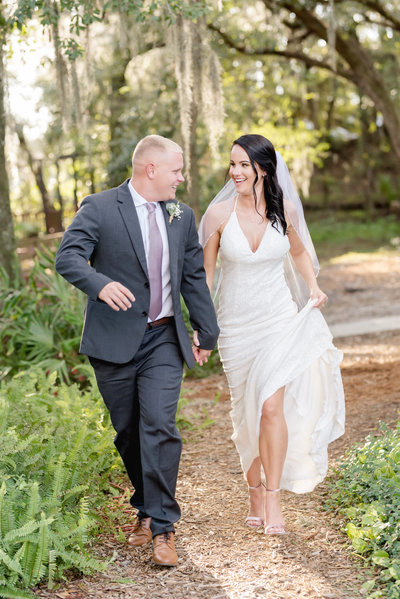 Bride and groom hold hands while running through nature on their wedding day