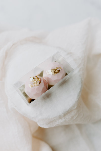 Two boxed chocolate covered truffles in pink with gold leaf.