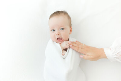 Baby mit blauen Augen in einer weißen Decke. Hand der Mutter berührt die Babyhand.