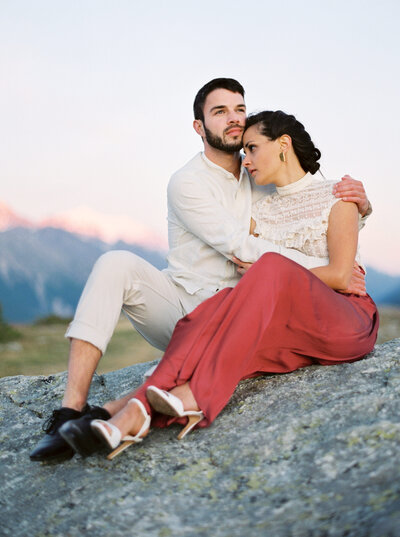 Man embraces his girlfriend while sitting on a rock