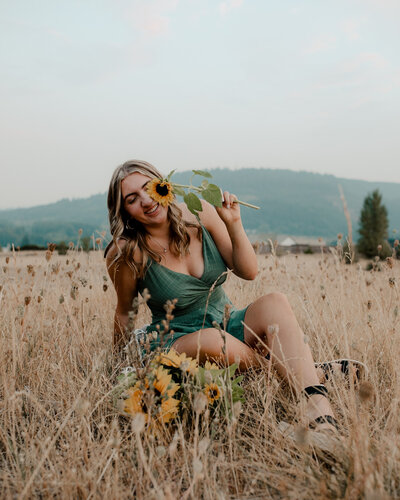 Senior girl sits in a field while holding sunflowers in her senior picture
