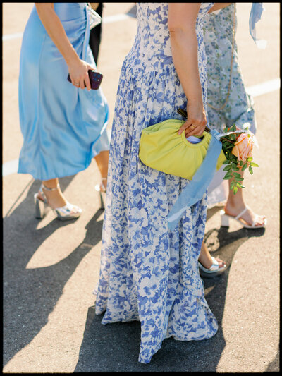 Bridesmaids in mismatched blue pattern dresses walk together during a wedding at Longboat Key Club while holding a yellow purse.