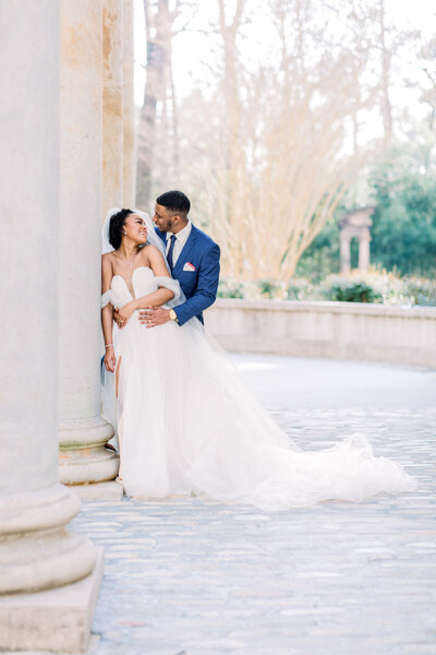 Luxury wedding portrait beneath grand columns in Atlanta at Swan House Bride and groom smiling at each other beneath elegant stone columns during a luxury Atlanta wedding portrait session