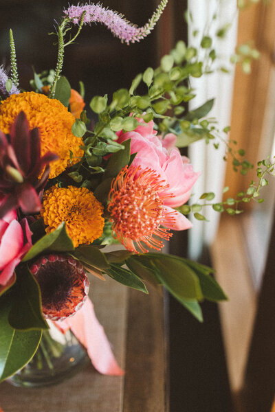 Bouquet of coral charm peony, pincushion protea, penny cress and marigolds on a table at  Sunriver Great Hall