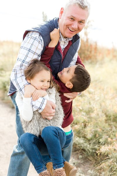 Kids playfully hang off of father's arms during family photography session in Edina.