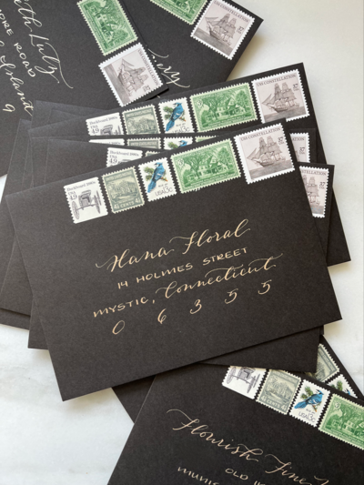 Black wedding invitation envelope with metallic ink calligraphy and vintage postage stamps.