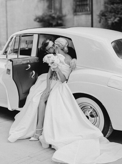 Bride in off the shoulder gown with long white train kisses her groom while in vintage car at wedding at Castle and Key Distillery in Lexington Kentucky photographed by Lexington Kentucky wedding photographer Magnolia Tree Photo Company