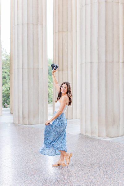 Nashville Wedding Photographer Brooke Elliott wearing an off-the-shoulder white tank top and a blue floral skirt twirls around at the War Memorial in Nashville Tennessee.