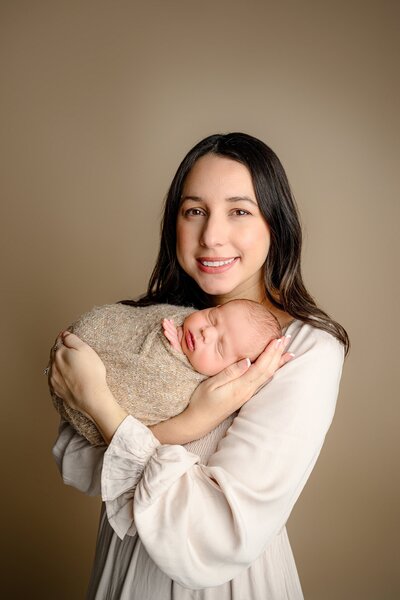 charlotte mom holds her newborn son wrapped in a brown wrap in a family studio session