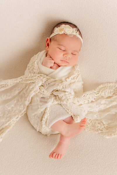 Newborn portrait with white lace wrap and neutral background.