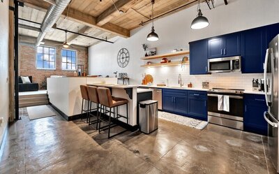 Kitchen with bar height seating and open beam ceiling in this three-bedroom, two-bathroom industrial modern loft condo in the historic Behrens building in downtown Waco, TX.