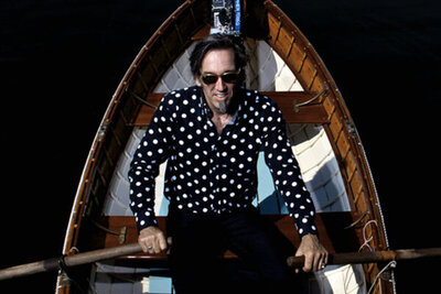 Musician portrait of Stephen fearing high angle perspective as he sits in rowboat holding oars in either hand wearing black and white polkadot shirt